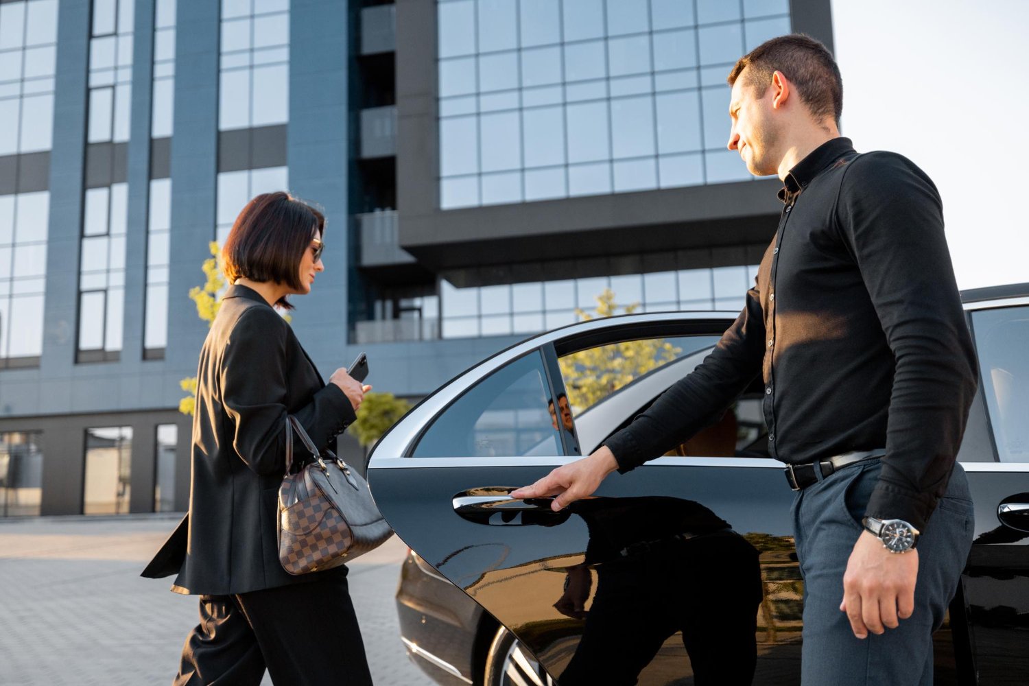 A man and woman are entering a black car, preparing to drive away together.